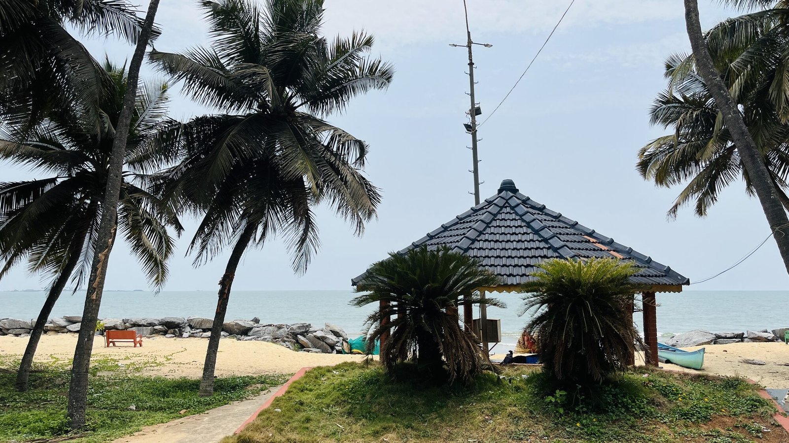 Traditional tiled hut on Malpe beach among palms