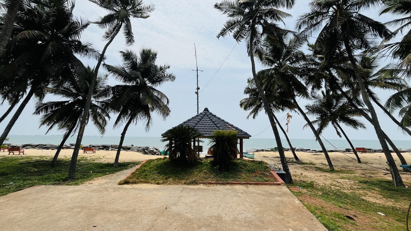 Traditional tiled hut on Malpe beach among coconut palms